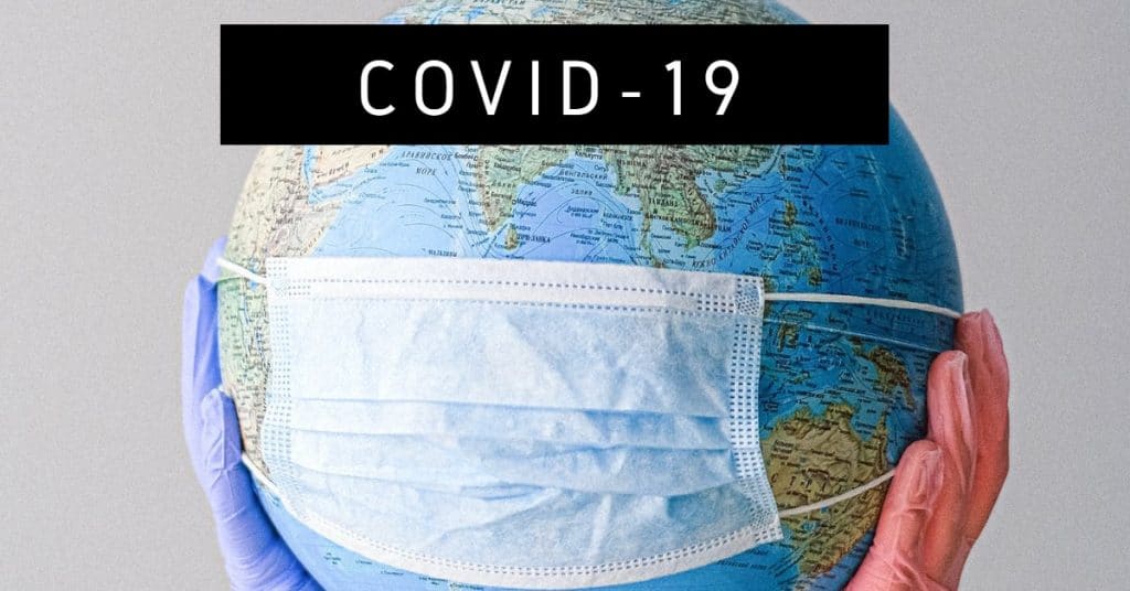 Photo of globe with a surgical mask held up with latex gloves and the words "covid-19"