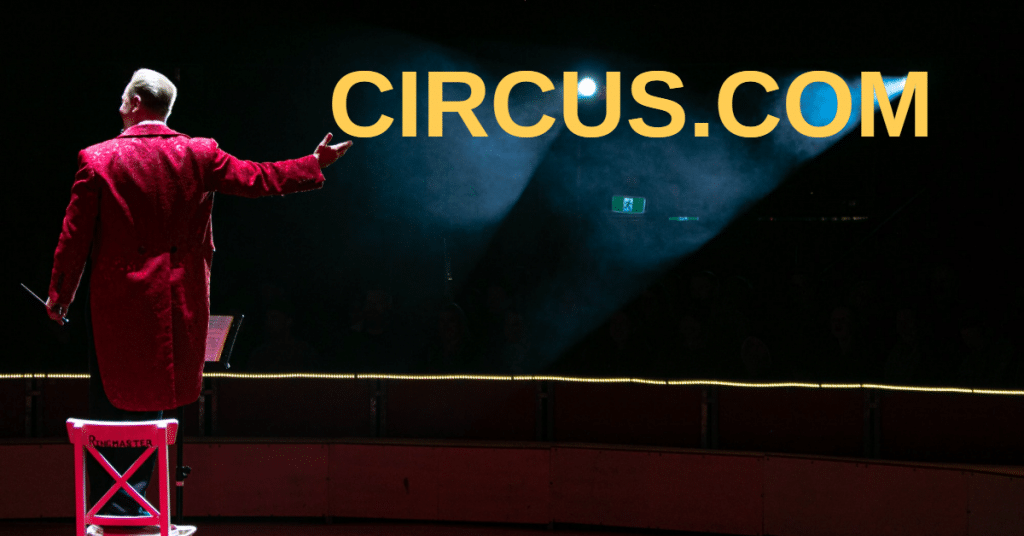 Picture of a circus ringmaster in a red coat standing on a chair, with a hand outstretched and the word circus.com in yellow letters