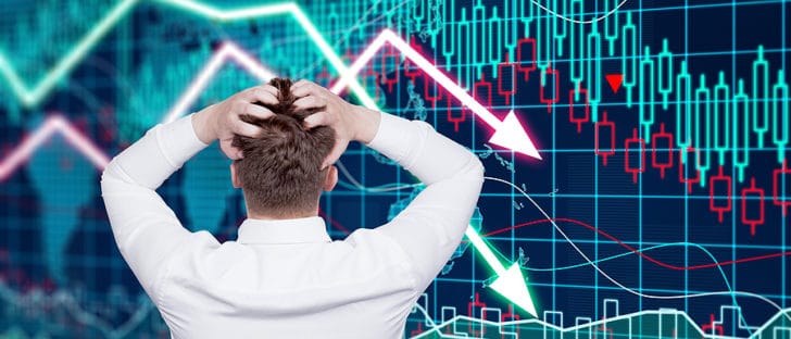Picture of man with hands in hair watching downward arrows representing market prices