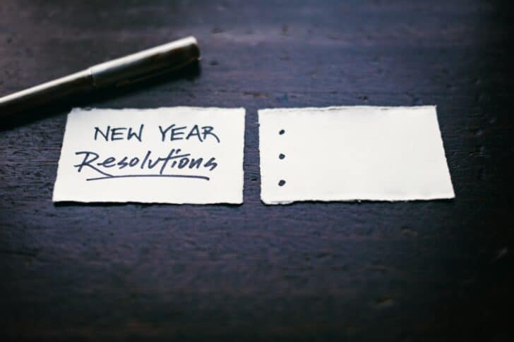 Two scraps of paper. The left one has "New Year Resolutions" written, and the right one has three bullet points that are blank.